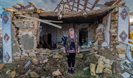 En kvinna står utanför sitt sönderbombade hem i Ukraina.
