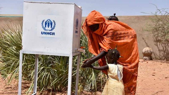 En kvinna och ett barn på flykt från Sydsudan tvättar händerna för att hindra spridning av covid-19 innan de registreras i ett flyktingläger i Södra Darfur.