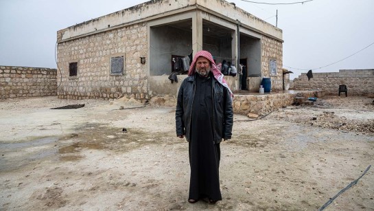 En man står på gården framför sitt hem i Syrien.