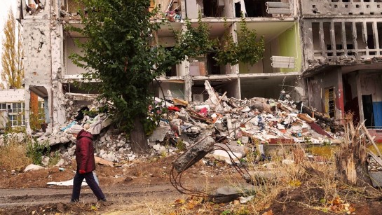 En kvinna går förbi ett sönderbombat flerfamiljshus i Saltivka i östra Ukraina.
